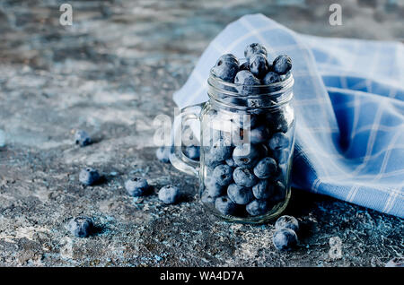 Les bleuets mûrs dans un bocal en verre avec des feuilles menthe sur un fond de béton foncé Banque D'Images