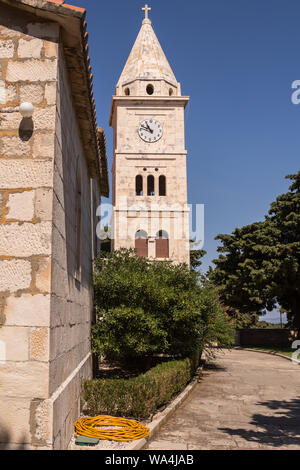 Église de Saint George, situé sur une colline, entouré d'un parc et des bâtiments en pierre. Ciel bleu d'été. Tour avec réveil et une croix. Primosten, Croatie. Banque D'Images