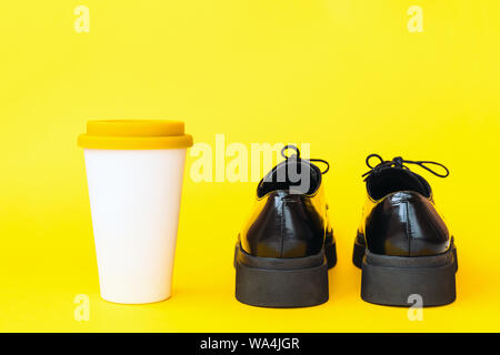 Des bottes noires et une tasse en bambou avec un couvercle en plastique pour le café d'aller Banque D'Images