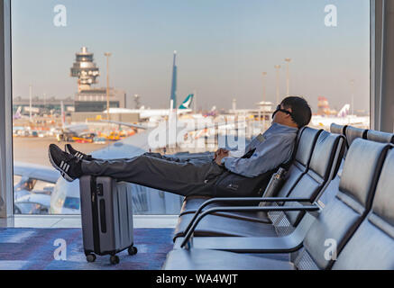 De l'aéroport de Hong Kong, Hong Kong - Octobre 29th, 2018 : Une jeune femme dormir sur place à l'aéroport de Hong Kong, reposant ses pieds sur sa valise. Banque D'Images