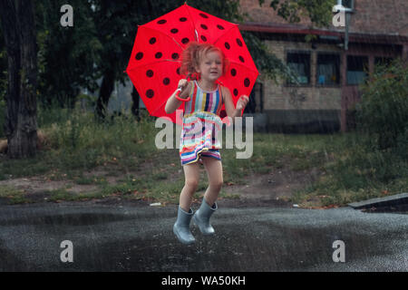 Little girl with umbrella jumping dans la pluie à travers les flaques. Banque D'Images