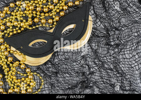 Masquerade ou Halloween fond avec un chat noir et un masque de style masque métallique or et perles dorées sur un fond de compensation Banque D'Images