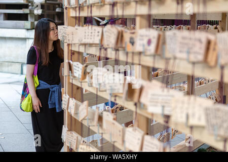 Tokyo, Japon - 14 juin 2015 - Une femme asiatique ressemble à l'ema, tablettes en bois japonais désireux, pendaison sur racks dans temple à Tokyo, au Japon, le Ju Banque D'Images