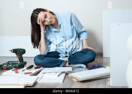 Assez jeune femme assise sur le sol en face des meubles, ne peut pas collecter des meubles de salon Banque D'Images