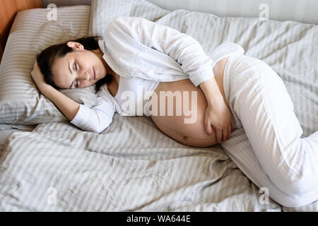 Dormir enceinte femme couchée sur le lit avec sa main sur son estomac dans le dernier mois de la grossesse Banque D'Images