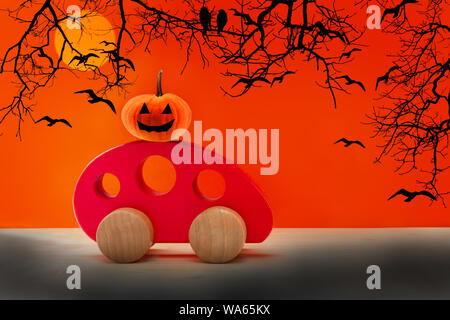 Voiture jouet en bois rouge porte une citrouille effrayant. Happy Halloween concept Banque D'Images