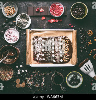 Préparation de l'Écorce au chocolat maison avec divers garniture : chocolat fondu dans des bols , spatule, écrous, guimauve, réglisse, noix, caramel et cand Banque D'Images