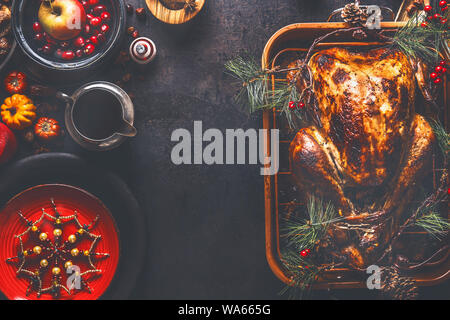 Le dîner de Noël arrière-plan. Dinde farcie rôti servi avec des canneberges fraîches, des branches de pins et la sauce sur fond rustique avec plaque rouge, snowfl Banque D'Images
