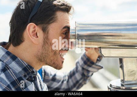 Side view portrait of smiling man à la recherche dans des jumelles à plate-forme d'observation, copy space Banque D'Images