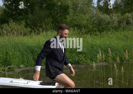 Jeune homme paresseux millénaire fatigué de travail ennuyeux. Se sent stressée et quitte le lieu de travail. Va dans un marais, dans l'eau Banque D'Images