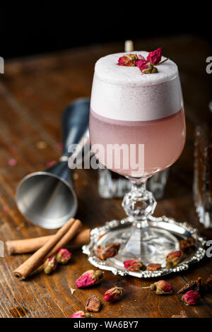 Cocktail sans alcool rose avec mousse, décoré de roses sèches. verre sur fond de bois. barman attributs sont à côté de l'autre. La vie nocturne dans un b Banque D'Images