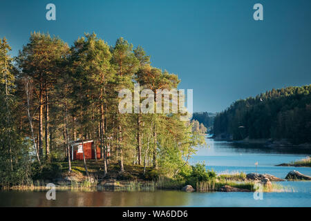 La Suède. Beau Chalet en bois suédois rouge maison sur l'île Rocky Coast en été ensoleillé le soir. Paysage du lac ou de la rivière. Banque D'Images