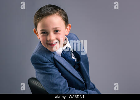 Portrait de 8 ans habillé en costume assis à l'arrière sur l'épaule et sourire isolé sur fond gris Banque D'Images