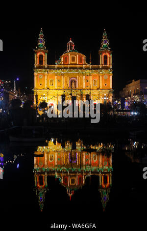 L'église paroissiale à Msida, Malte, avec façade illuminée pour la fête de saint Joseph et se reflètent dans l'eau de Msida Creek Banque D'Images