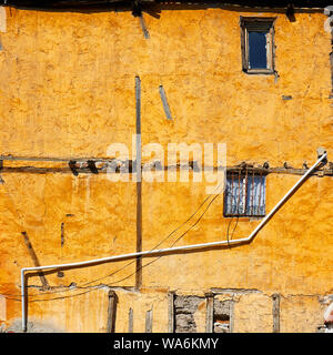 Old weathered façade d'une maison jaune avec vintage fenêtres avec grilles en fer forgé et un tuyau d'eau en pvc Banque D'Images