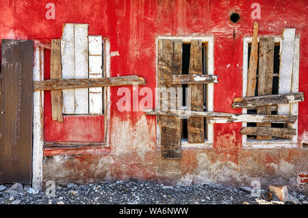 Close up vue extérieure d'une cabane abandonnée maison avec trois fenêtres et mur rouge barrée avec planches en bois Banque D'Images