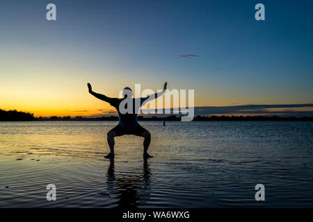 Lever du soleil silhouette d'un homme debout dans l'eau peu profonde et en pratiquant des mouvements de tai chi ou chigong, Boyd Lake State Park dans le nord du Colorado Banque D'Images