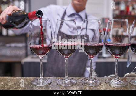 Barman verse du vin rouge dans des verres à vin d'une bouteille Banque D'Images