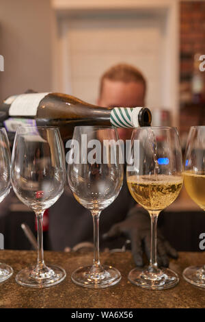 Barman verse du vin blanc dans des verres à vin d'une bouteille Banque D'Images