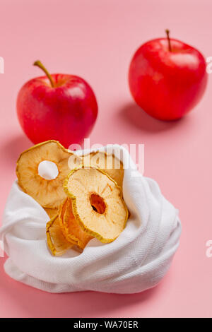Des produits biologiques séchées copeaux de pomme croustillante dans sac de tissu, sur fond rose des saveurs de pomme. Zéro déchets en plastique, textile recyclé libre concept. Co Banque D'Images