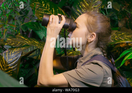 Traveler fille parmi la forêt tropicale se penche sur la distance avec des jumelles Banque D'Images