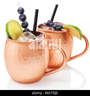 Froid glacial Moscow mule cocktail avec de la bière au gingembre, de vodka, de chaux et de bleuets dans des tasses en cuivre avec réflexion isolé sur fond blanc Banque D'Images