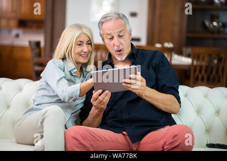 D'âge mûr à l'aide d'une tablette numérique sur leur canapé à la maison Banque D'Images