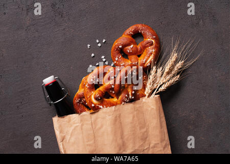 Bretzels salés frais et bouteille de bière dans le sac en papier sur la table marron décorée avec les épis de blé, la composition Vue de dessus Banque D'Images