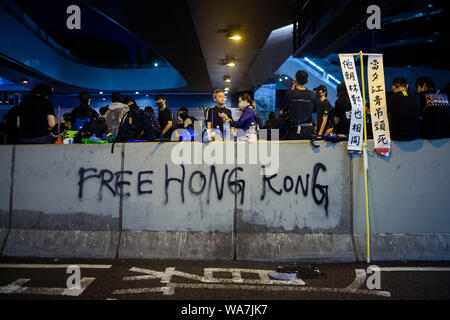 Hong Kong, Chine. 18 août 2019. Dans la soirée, les manifestants s'asseoir sur un mur décrit avec un graffiti ('gratuitement Hong Kong'). Dans l'ancienne colonie britannique de Hong Kong, les protestations contre l'influence de Beijing sont entrés dans un nouveau cycle. Le mouvement démocratique a appelé à une autre grande manifestation. Dpa : Crédit photo alliance/Alamy Live News Banque D'Images