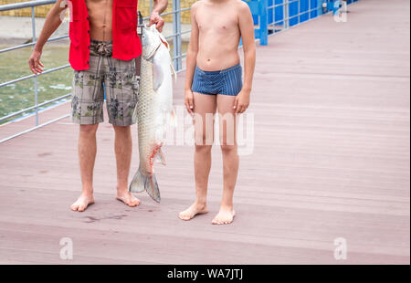 Fisherman holding une énorme carpe sur un quai sur un lac, debout avec son fils Banque D'Images