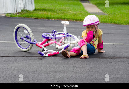 Une petite fille en équipement de sécurité, se trouve au milieu d'un trajet après avoir chuté de sa nouvelle moto. Banque D'Images