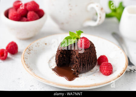 Gâteau au chocolat avec de la lave en fusion sur la plaque de base blanc servi avec des framboises fraîches et feuille de menthe Banque D'Images