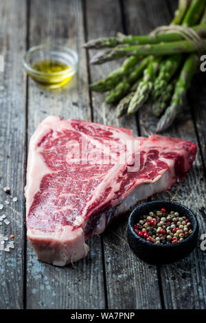 Matières T-bone steak avec des herbes fraîches et de l'huile sur fond de bois foncé Banque D'Images