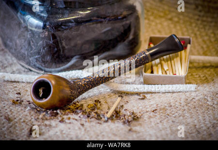 Tuyau d'artisan avec le tabac à cigarettes, allumettes et nettoie-pipe sur une toile de jute Banque D'Images