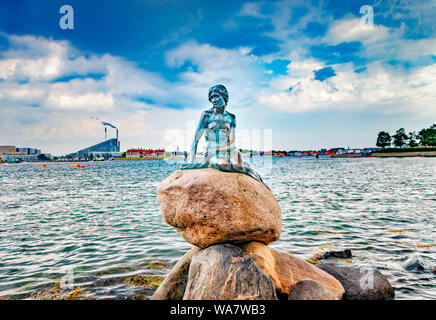 Statue de la petite sirène assise sur la pierre. Derrière c'est la mer et la vue sur le port de Copenhague. Banque D'Images