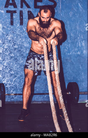 Formation Crossfit. Jeune homme barbu l'élaboration avec des cordes à la salle de sport de combat Banque D'Images
