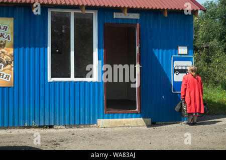 La Russie, le 16 août - DÉMIANSK, 2019, Femme au manteau rouge examine les horaires de bus au magasin rural Banque D'Images