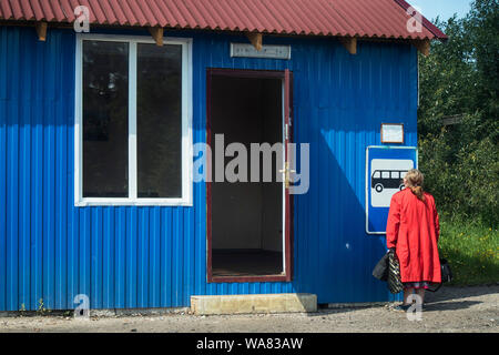 La Russie, le 16 août - DÉMIANSK, 2019, Femme au manteau rouge examine les horaires de bus au magasin rural Banque D'Images