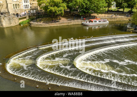 BATH, ANGLETERRE - Juillet 2019 : en forme de fer à cheval Le Pulteney Weir sur la rivière Avon, dans le centre de Bath. Un bateau de tourisme est en arrière-plan. Banque D'Images