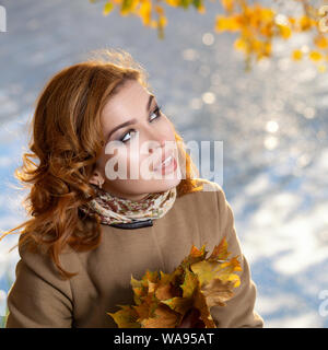 Jeune femme séduisante en manteau beige est debout dans le parc et détient l'automne jaune feuilles d'érable. Banque D'Images