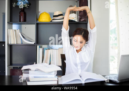 Asian woman stretching après la lecture de livre et travailler fort et souriant dans le home office Banque D'Images