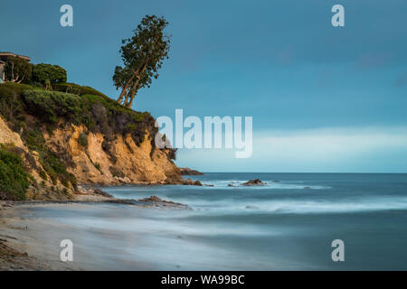 Belle longue exposition photo de petit Corona del Mar plage au coucher du soleil avec des vagues de lave en douceur sur le rivage et un arbre penché sur le bord d'un tal Banque D'Images