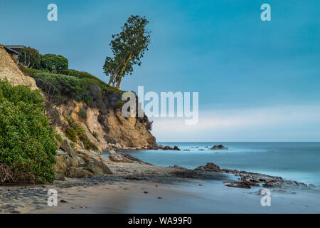 Belle longue exposition photo de petit Corona del Mar plage au coucher du soleil avec des vagues de lave en douceur sur le rivage et un arbre penché sur le bord d'un tal Banque D'Images