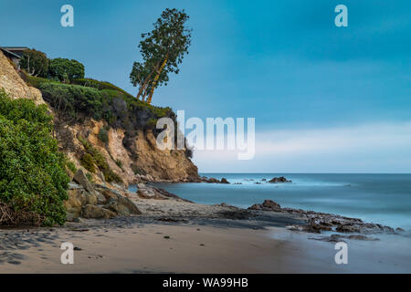 Belle longue exposition photo de petit Corona del Mar plage au coucher du soleil avec des vagues de lave en douceur sur le rivage et un arbre penché sur le bord d'un tal Banque D'Images