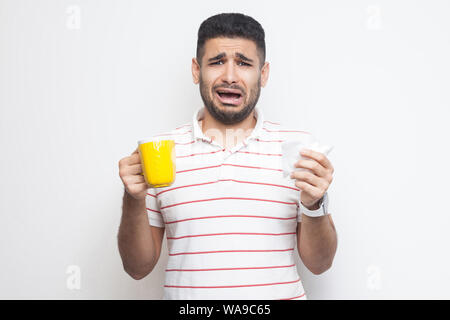 Retrouvez des jeunes adultes malades malheureux homme en blanc T-shirt debout et tenant de la coupe jaune avec serviette blanche, boire du thé chaud, a la grippe. Piscine, isolé, blanc Banque D'Images