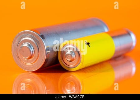 Utilisé seul AA et seule pile alcaline AAA sont vus sur une surface réfléchissante orange. Côté Gros plan vue depuis le plus côté de la batterie. Banque D'Images