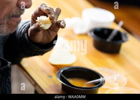 Homme âgé mange de la soupe chaude avec du pain dans une cuisine avec de la nourriture gratuite pour les pauvres et les sans-abri. Banque D'Images