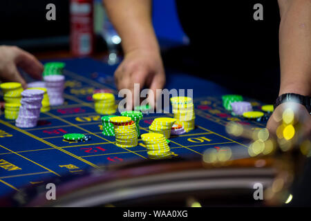 Table de roulette avec des mains de poser des jetons dans un casino. La roue de roulette à l'avant-plan. Jouer jeu. Les gens méconnaissables. Banque D'Images
