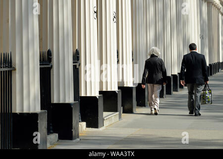 Couple walking cours des colonnes en stuc, Eaton Square, garden square, Belgravia, à l'ouest de Londres, Royaume-Uni Banque D'Images