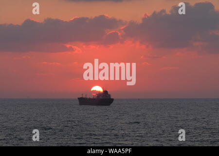 Coucher de soleil sur la mer Méditerranée à travers rose bleue/chimique pétrolier construit en Chine navigation au large en Israël Banque D'Images